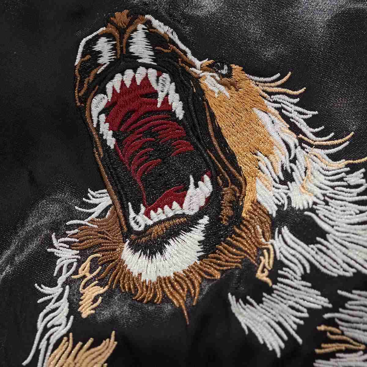 Embroidery close-up — open-mouth lion with dense stitches and shading.