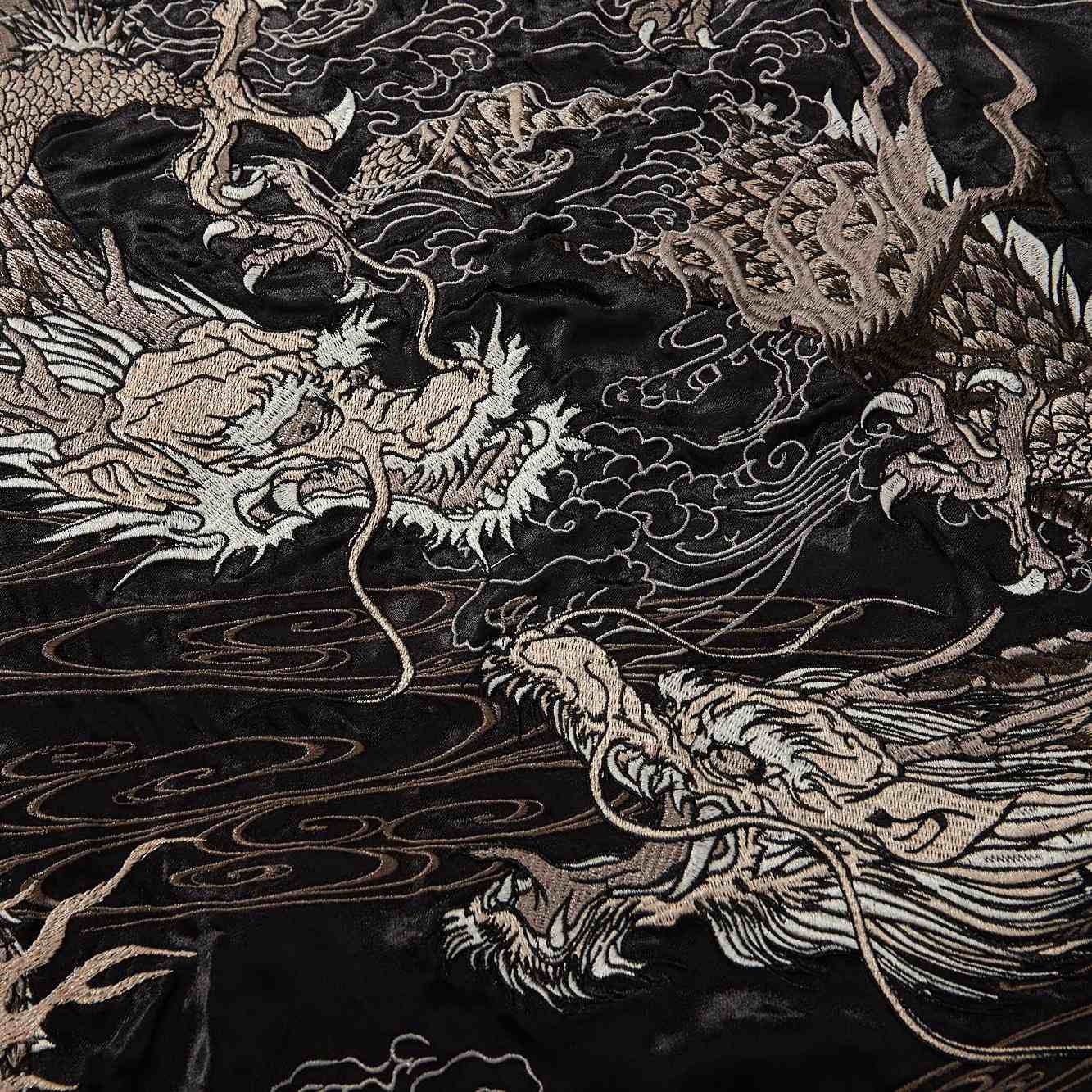 Embroidery close-up — intertwined dragons rendered with layered metallic threads.
