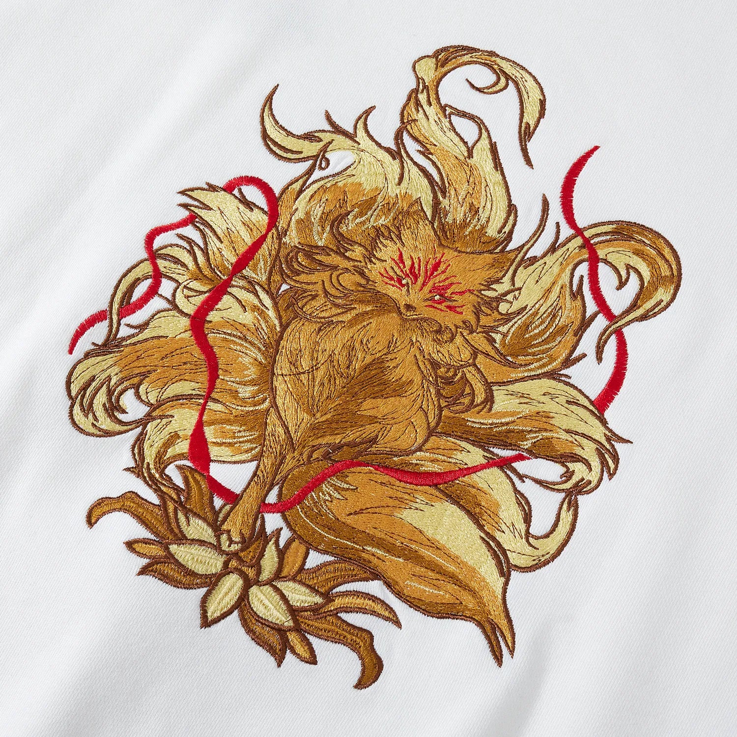 Close up of large nine-tailed fox and lotus embroidery with red ribbons on back of white sweatshirt.