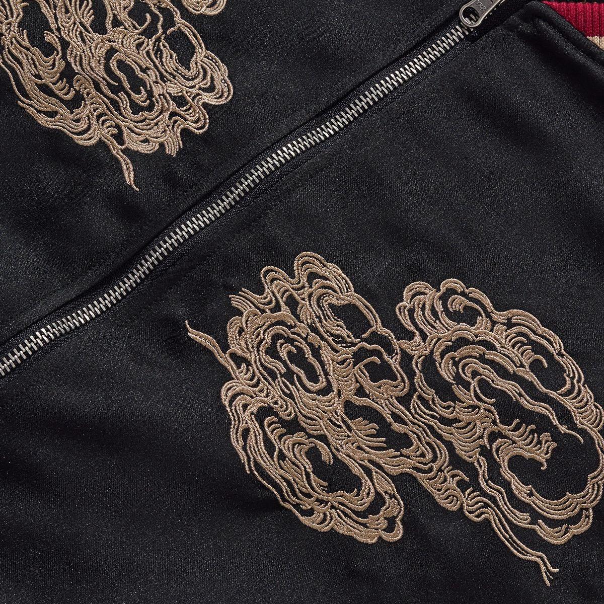 Chest embroidery of twin swirling clouds beside the front zipper, close-up