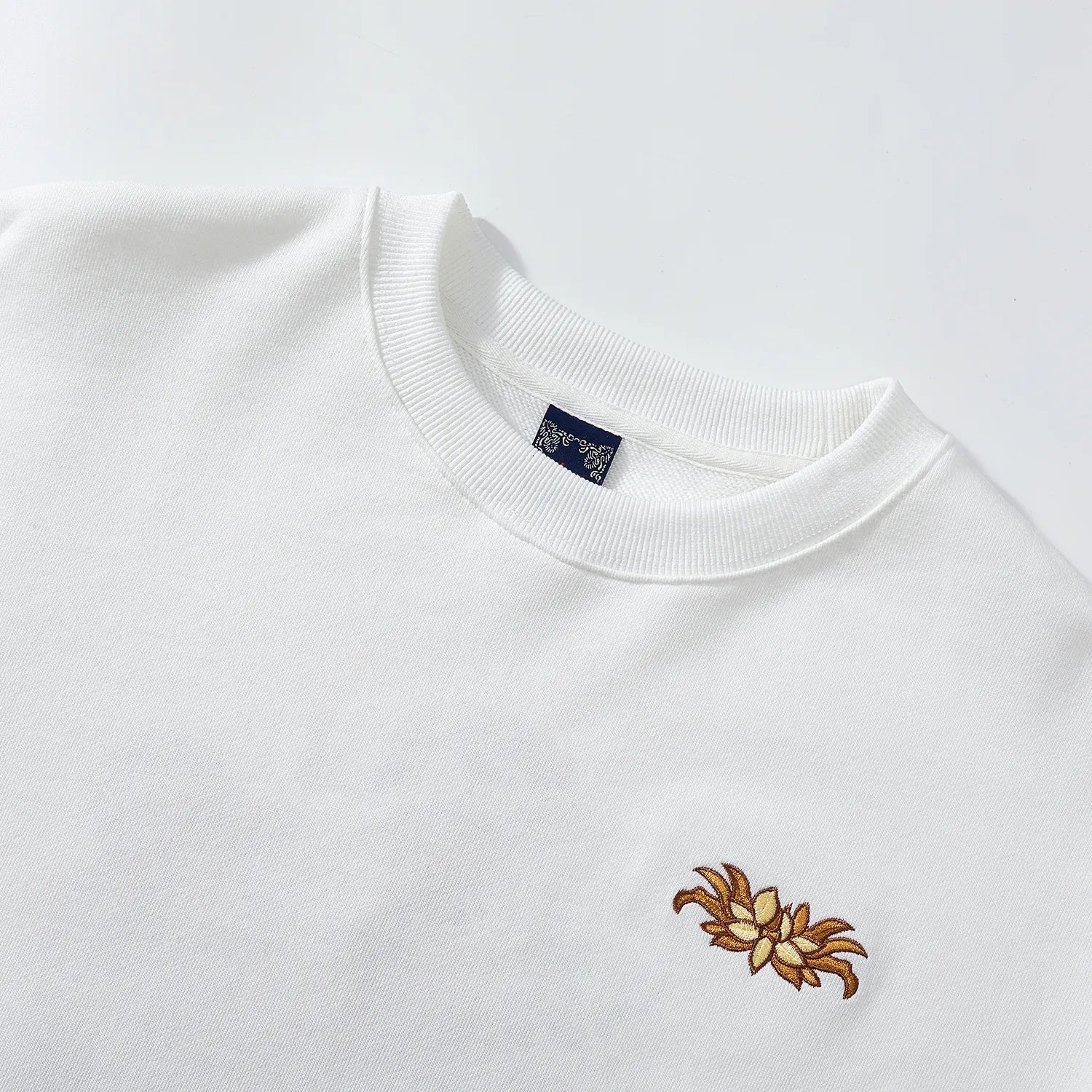Close up of crewneck and front lotus chest embroidery on white Nine-Tailed Fox & Lotus sweatshirt.