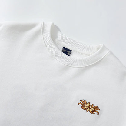 Close up of crewneck and front lotus chest embroidery on white Nine-Tailed Fox & Lotus sweatshirt.