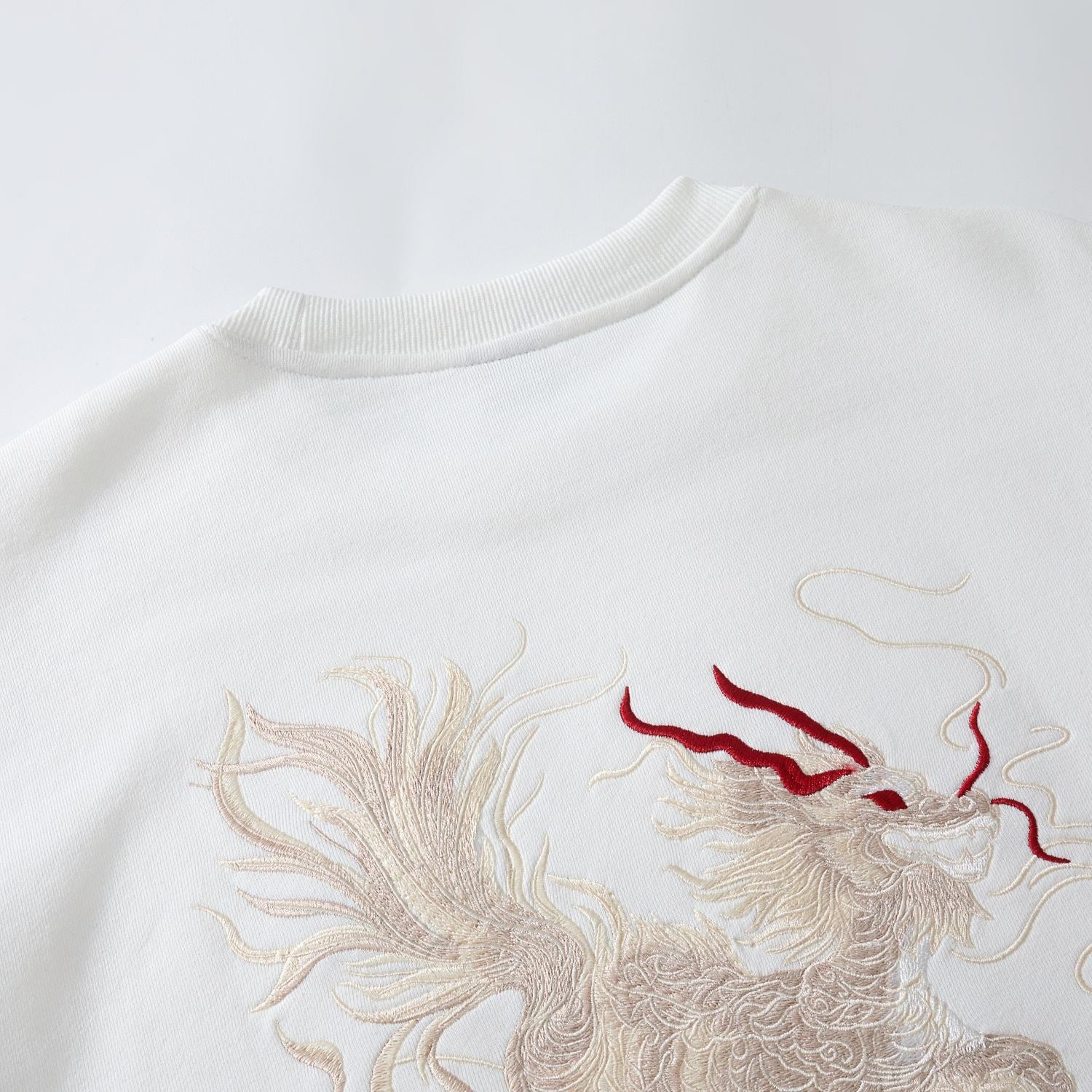 Back collar close-up of the white Kirin & Lotus Embroidered Sweatshirt showing flowing Kirin stitching and ribbed neckline
