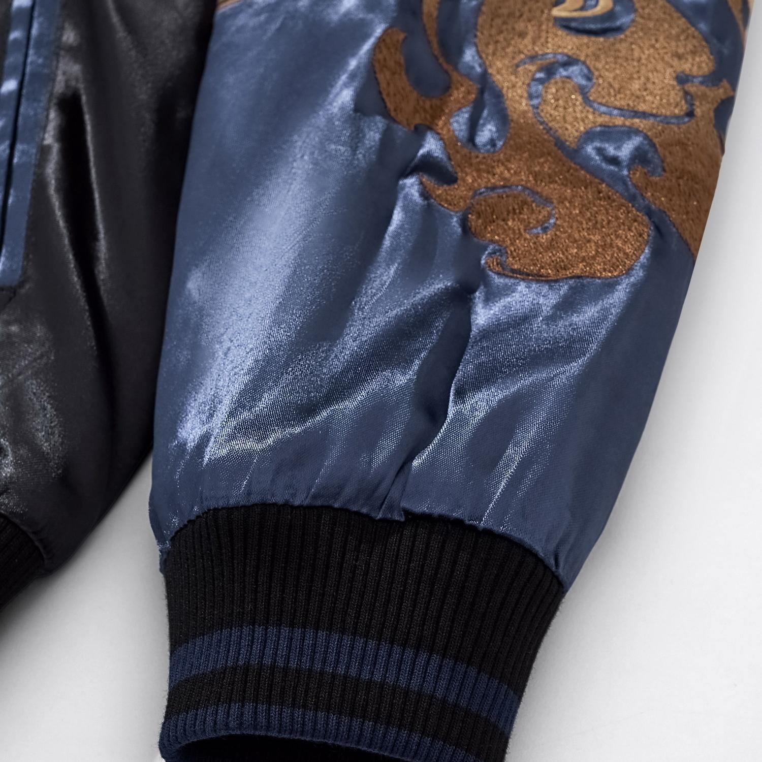 Detail shot of gold spirit flame embroidery on the blue satin sleeve near the black ribbed cuff.