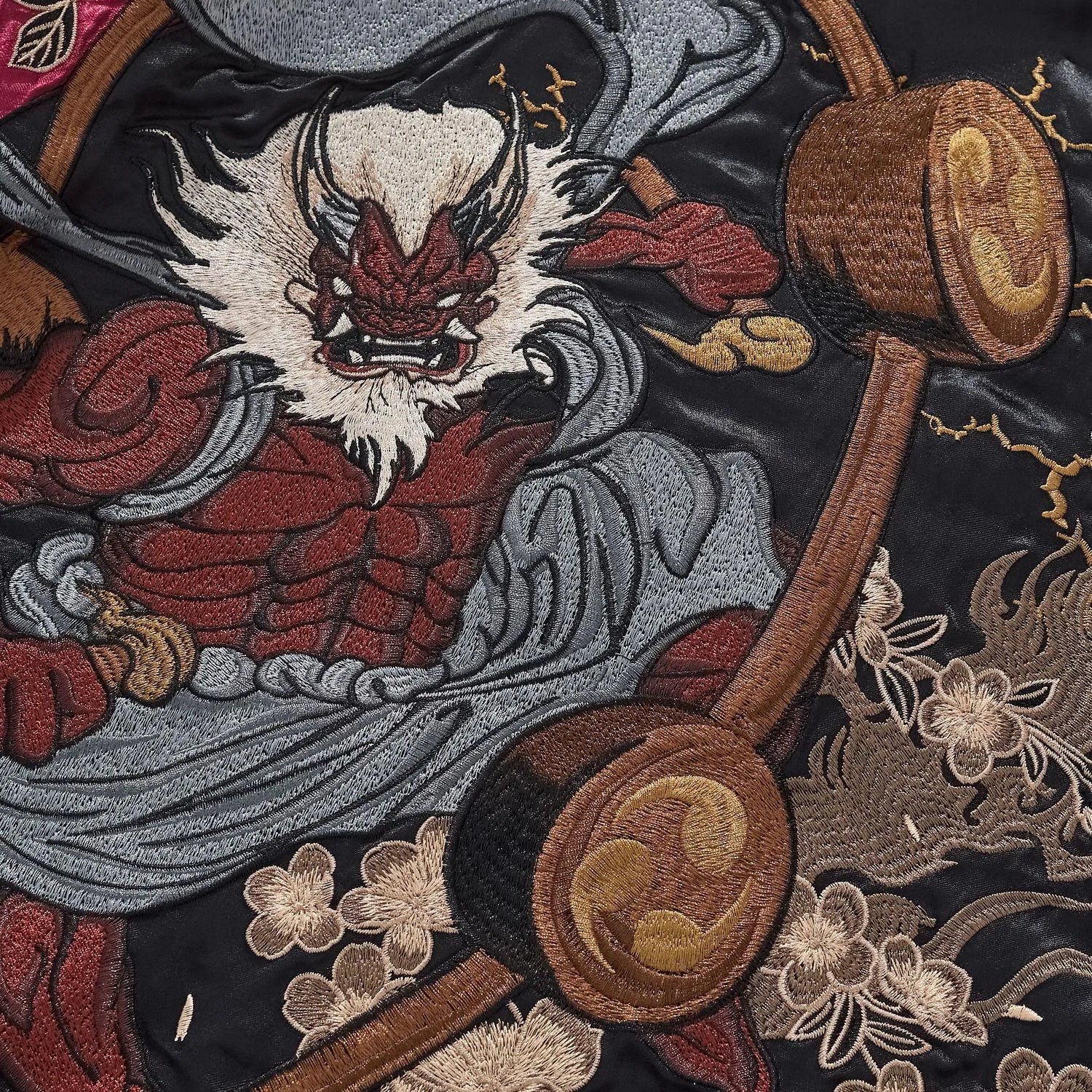 Extreme close-up of the Red Thunder God (Raijin) face embroidery on the burgundy jacket.