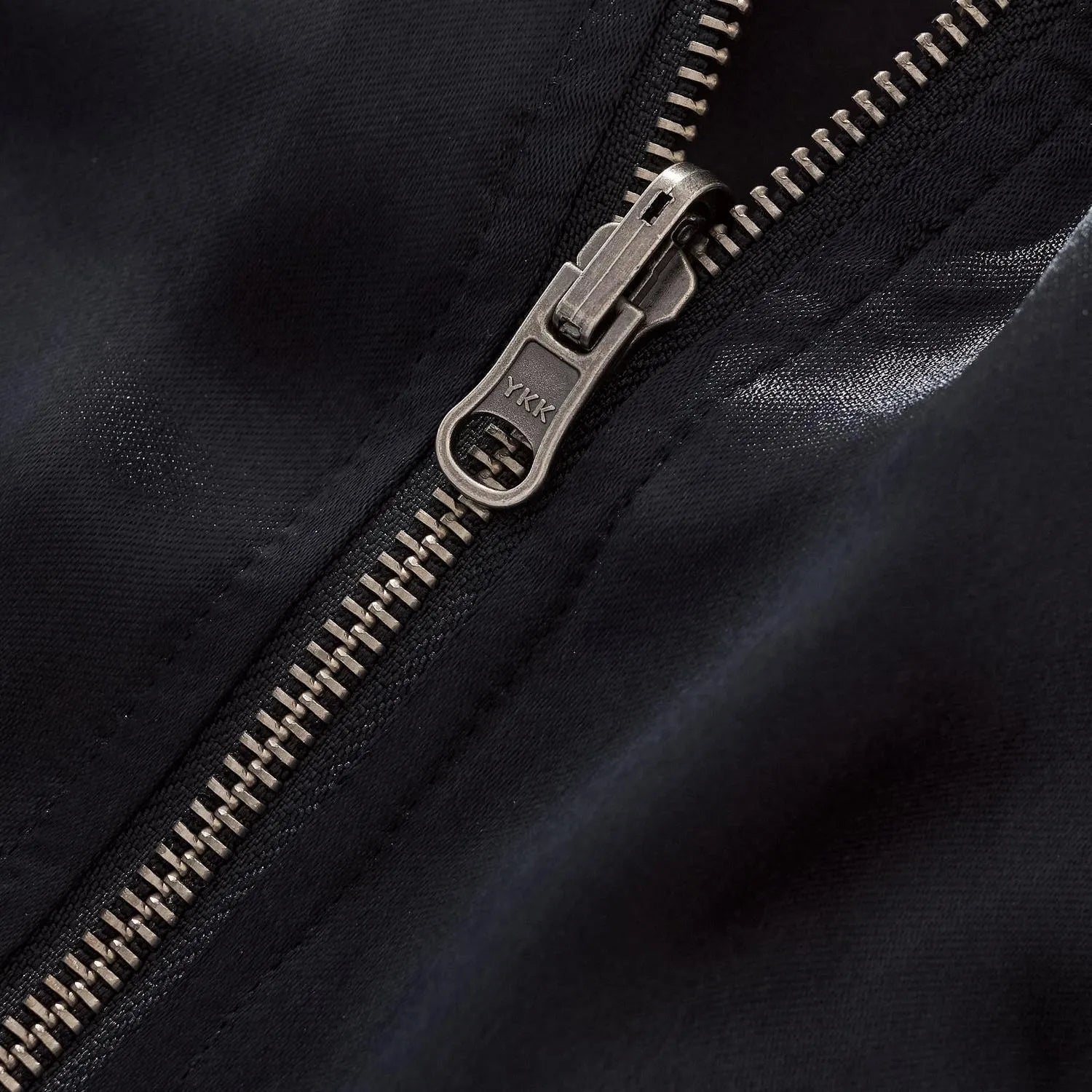 Macro photography of the antique silver YKK zipper pull on black rayon fabric.