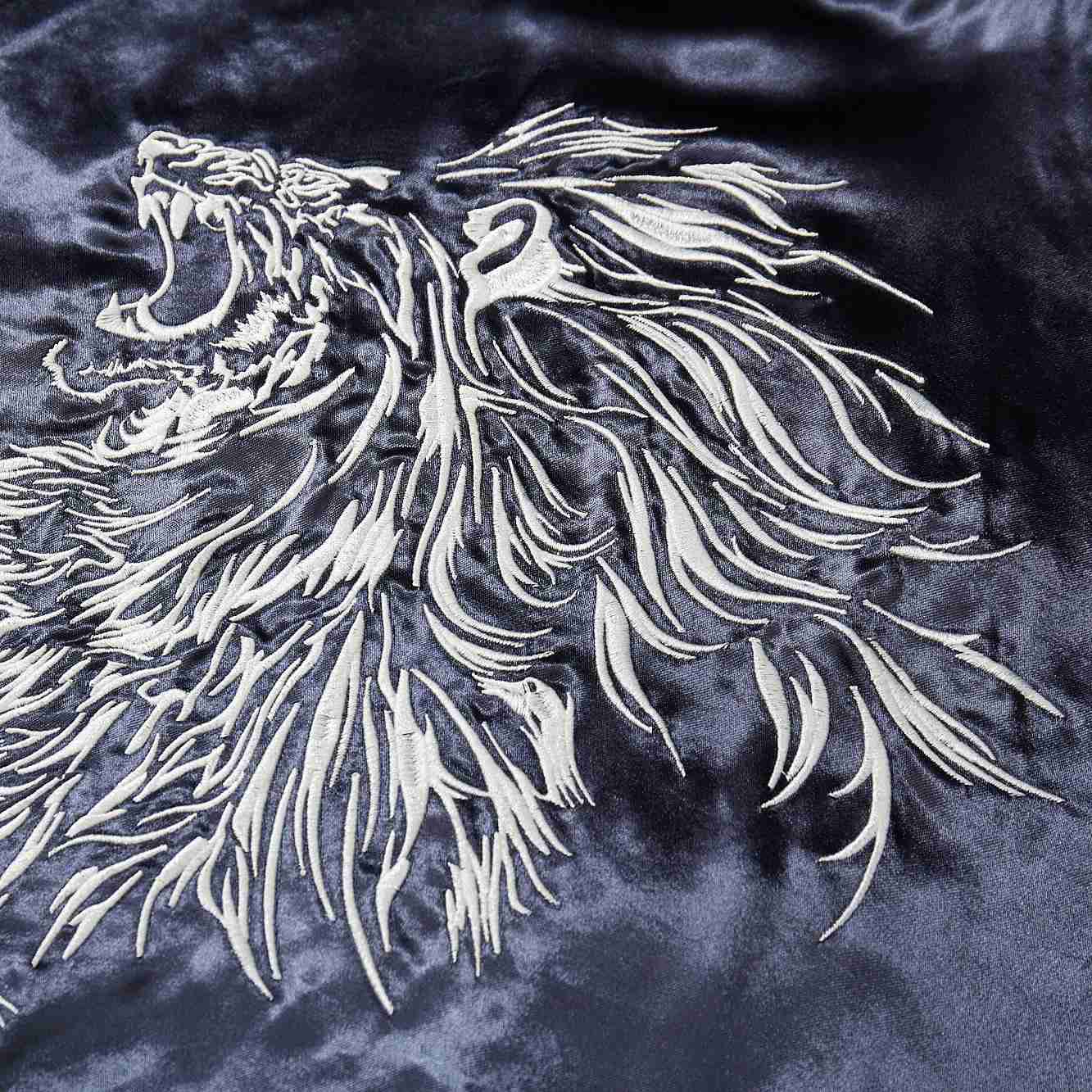 Close-up of the white lion’s flowing mane embroidery on navy satin.
