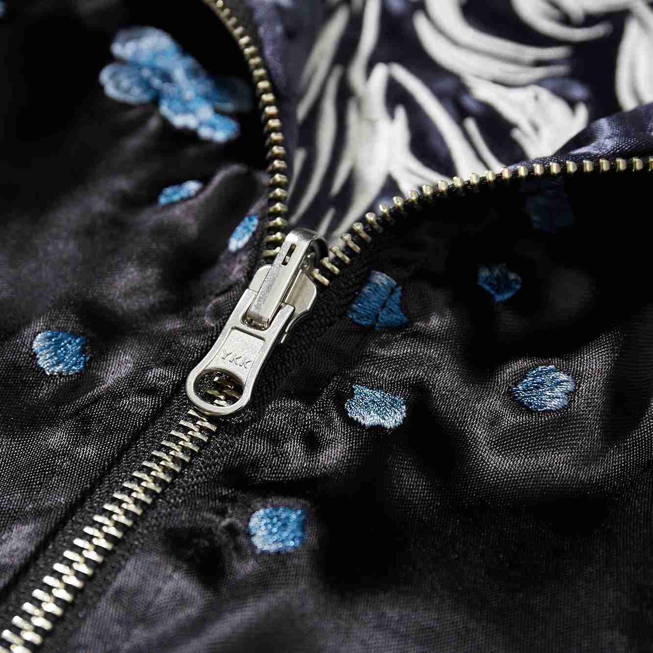YKK metal zipper close-up with scattered blue blossom embroidery.